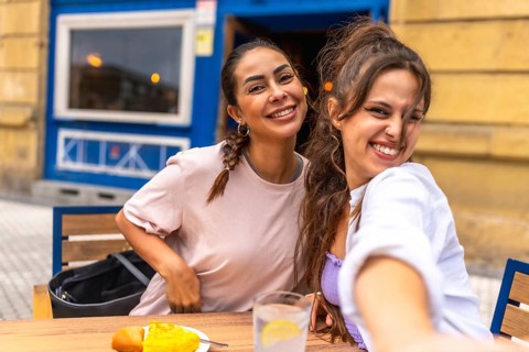 Two friends are taking a selfie while enjoying breakfast at an outdoor cafe, capturing a moment of