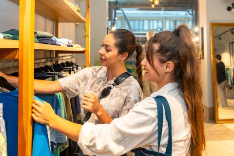 Two young women looking and choosing clothes in a fashion store, the shop assistant is helping a