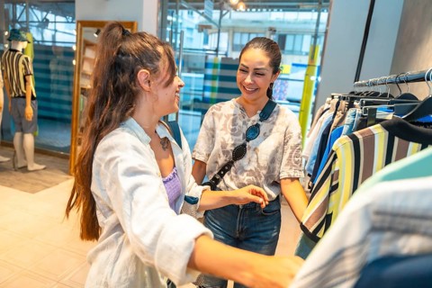 Two female customers smiling and chatting while selecting fashionable clothes in a vibrant retail