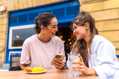 Two women are enjoying a meal and drinks at an outdoor cafe, sharing a moment of connection as they