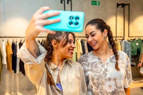 Two happy women taking a selfie with a smartphone in a clothing store, enjoying shopping and trying