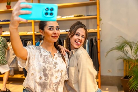 Two cheerful female customers taking a selfie with a smartphone, having fun and making funny faces