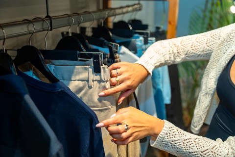 Female customer browsing through new collection in clothing store, selecting beige pants hanging on