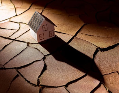 A cardboard miniature house placed on cracked, dry soil, illustrating drought, environmental