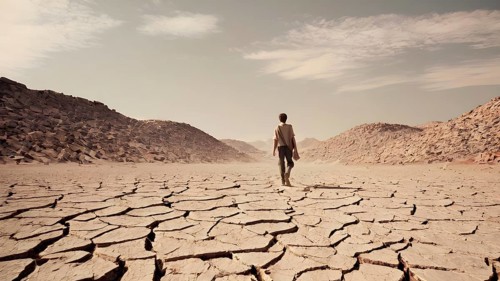 Man standing on dry cracked clay crust in desolate desert. Climate change and global warming. AI