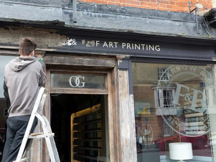 Decorator preparing wooden surface of shop front for painting, Devizes, Wiltshire, England, UK