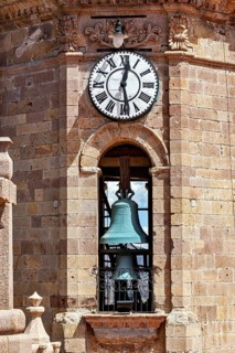 Detail of a clock tower with a large clock and a visible bell in a colonial building, The churches