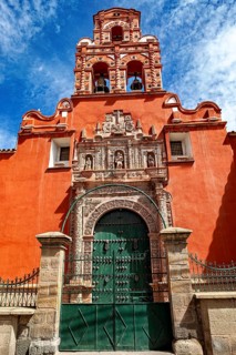 Door of a colonial building with red façade and bell tower under a clear blue sky, The churches of