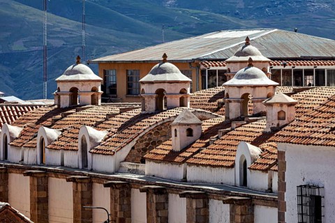 Close-up of building roofs with characteristic small domes and mountain scenery in the background,
