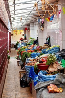A narrow and covered market aisle full of vegetables and spices, atmospherically colourful, market