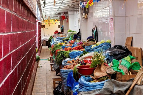 A covered market aisle full of colourful vegetables and spices in a tight arrangement, market stall