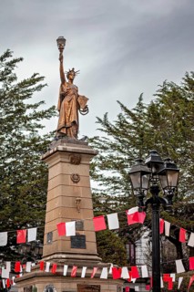 Historical statue with lantern on a high pedestal, surrounded by red and white flags and trees