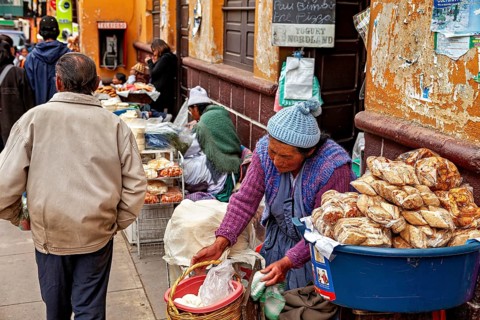 A woman sells bread at a busy street market as passers-by walk past, market stall selling goods in