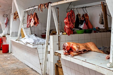 A rustic market stall with raw meat hanging on tiled walls, The meat market in the market halls of