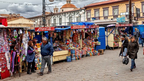 Colourful market stalls with Coca-Cola signs on a busy pavement full of people, Small market stalls