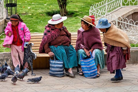 Two woman, two children on a park bench talking while pigeons are nearby, woman and people in the