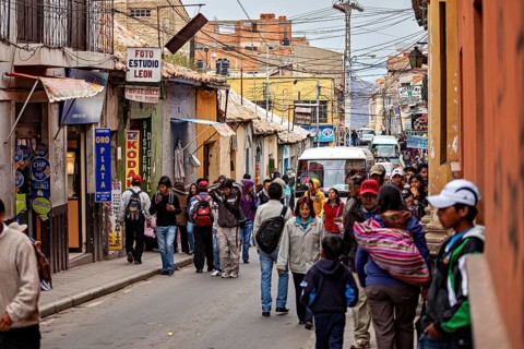 Lots of hustle and bustle in a narrow city street with people walking past. Various shops and
