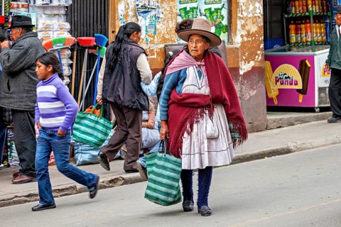 Woman in traditional clothes with bags walking past market stalls on the street, woman and people
