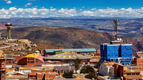 View over a city with colourful roofs and a telecommunications tower, surrounded by mountains under