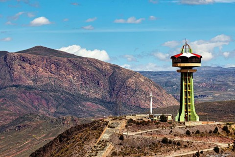 Observation tower next to cross and rocky mountain under blue sky with clouds, The water tower of