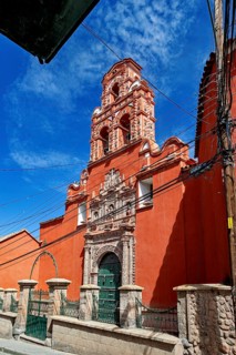 Colonial building with red façade and bell tower, surrounded by power lines and a clear sky, The