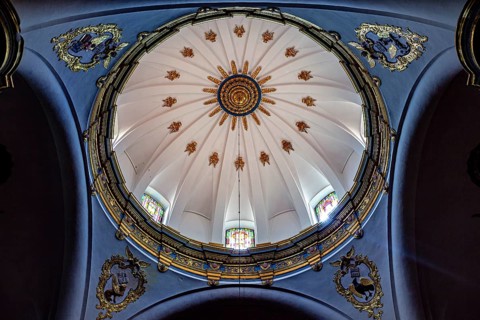 Dome of a church with golden decorations on a blue background and light through windows, inside the