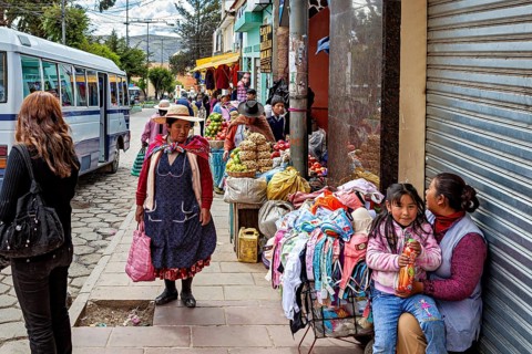 Street with vendors, fruit and clothes, busy with passers-by and a bus, people in the streets of