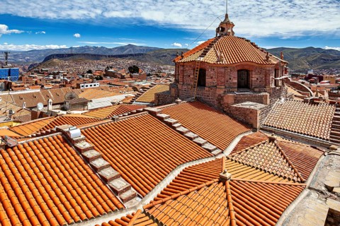 Red roof tiles of a city with colonial architecture, surrounded by mountains under a blue sky, The
