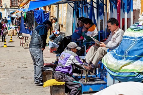 Lively street scene with people at a South American market, a shoeshine boy at work, shoeshine boy