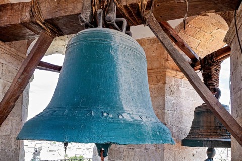 Two large bells hang in a historic bell tower with stone pillars and wooden beams, The large bell