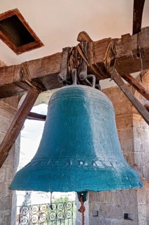 Large bell in an old tower made of wood and stone, with a bright sky in the background, The large