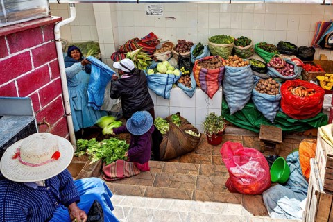 Women arranging vegetables in colourful sacks at a market stall in Bolivia, selling goods in the