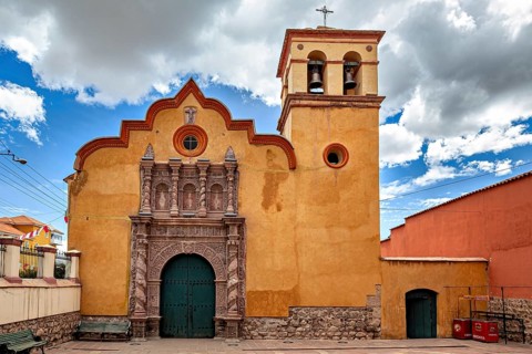 Colonial church with baroque bell tower and impressive wooden gate under a dramatic sky, The old