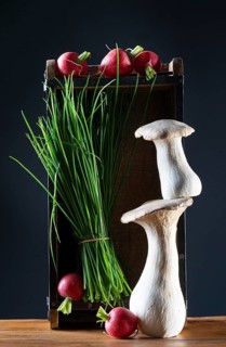 oyster mushrooms with radishes, chives and chillies on a wooden crate against a dark background