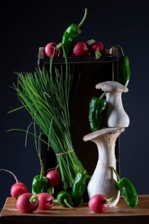 oyster mushrooms with radishes, chives and chillies on a wooden crate against a dark background