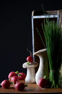 oyster mushrooms with radishes and chives in front of a wooden crate with a dark background