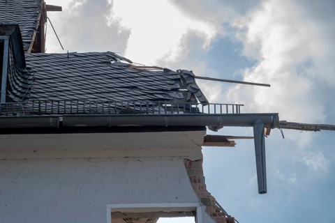 House roof with broken slate tiles and exposed framework showing destruction