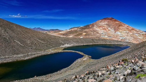 Volcanic mountain reflected in the lake, surrounded by barren landscape and under a bright blue