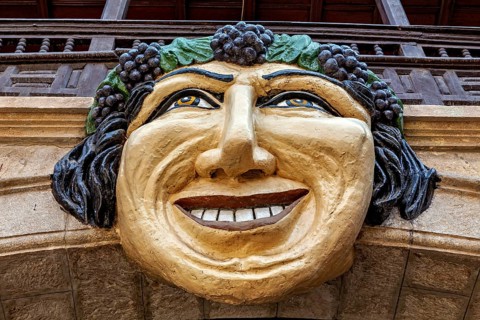 Stone mask with smiling face on an architectural structure, surrounded by green and brown tones,