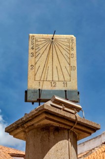 Stone sundial, mounted on a column, with dial and hands in front of a bright sky, The sundial of