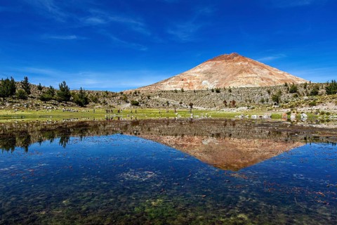 Volcanic mountain reflected in the calm waters of the lake under a clear blue sky, surrounded by