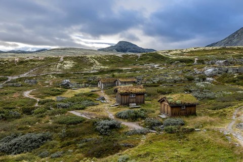 Wooden huts scattered in a forested mountain landscape with narrow paths and moderate cloud cover