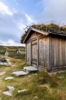 Wooden hut with grass roof and path in a rural setting under a blue sky with clouds, Peer Gynt