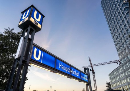 The picture shows a modern high-rise building in Berlin and a striking underground station sign