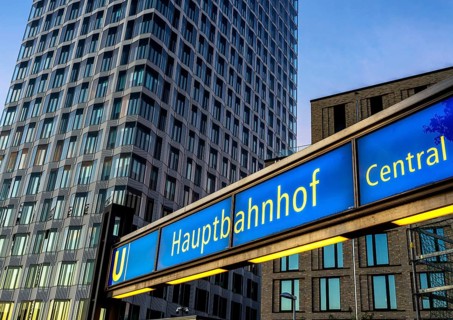 The picture shows a modern high-rise building in Berlin and a striking underground station sign