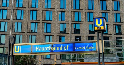 The picture shows a modern high-rise building in Berlin and a striking underground station sign