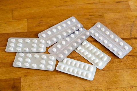 White medical tablets in foil blisters on wooden table top background, UK