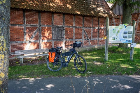 Bicycle in front of an old brick wall, next to it an information board in the sunshine, Weser cycle