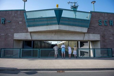 Four people stand in front of a modern lock structure made of concrete and blue railings, Minden