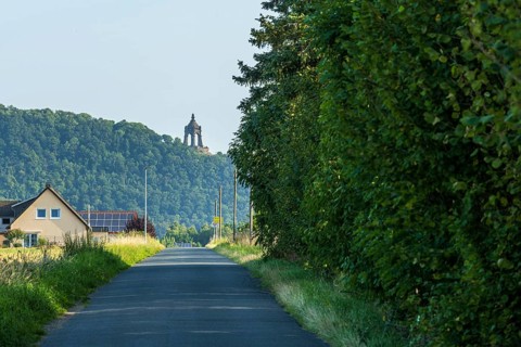 Landscape with a monument on a hill, surrounded by green trees and a house at the roadside,